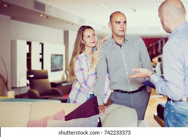 Man 40-45 Years Old And Woman 25-30 Years Old Are Consulting With Seller To Choose New Sofa For Home. 