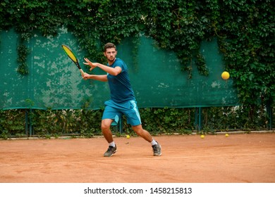 Man Is About To Hit A Ball Back With Forehand Shot. Young Tennis Player Practicing At Outdoor Court. Summer, Racket Sports.