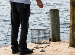 A Man Is About To Thrwo A Crab Trap With Chicken In It As Bait Into The Water Off Of A Wooden Dock.