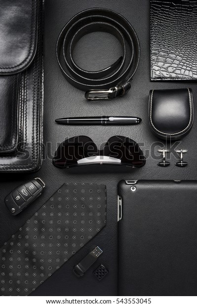 Man accessories\
in business style, silk tie, gadgets, briefcase, clothes and other\
luxury businessman attributes on leather black background, fashion\
industry, top view 