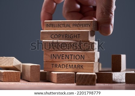 man adding a  block showing the words ’Intellectual property’ on top of  other wooden block with text copyright, patents,  invention,and trademark   