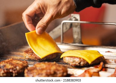 Man Adding Cheddar Cheese On The Top Of A Cooked Burger In A Barbecue