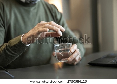 Man adding crumbling effervescent tablet into glass of water. Dissolving medicine for healthcare, wellness, and symptom relief