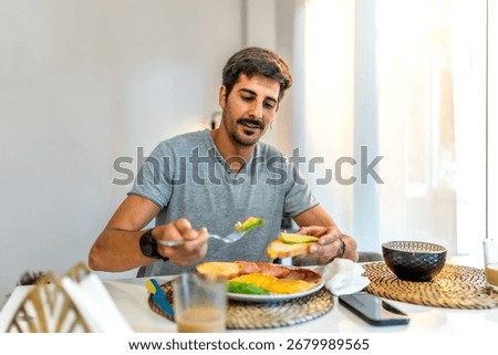 Man adding fresh avocado to toast while enjoying a healthy breakfast at home, embracing a balanced morning routine in a modern kitchen