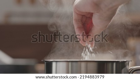 man adding salt to boiling water in saucepan, wide photo