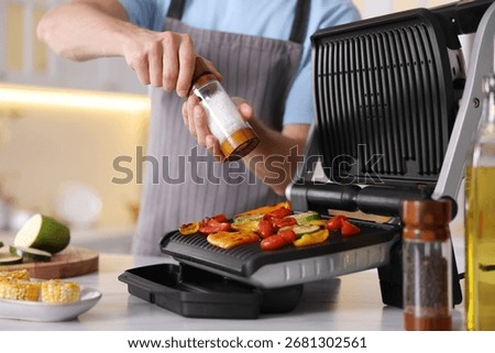 Man adding salt to vegetables cooking on electric grill in kitchen, closeup