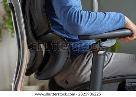Man adjusting the armrest while sitting in an ergonomic office chair with lower back support. Person adapting office chair for more comfortable sitting while working