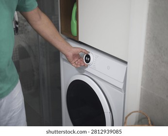 Man adjusting the control dial and choosing washing settings on a modern front-loading washing machine during a domestic laundry routine. Adjusting the Washer Dryer Control Knob