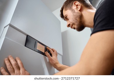 Man adjusting control panel on heat pump inside modern home during installation. Concept of home heating, energy efficiency and HVAC maintenance