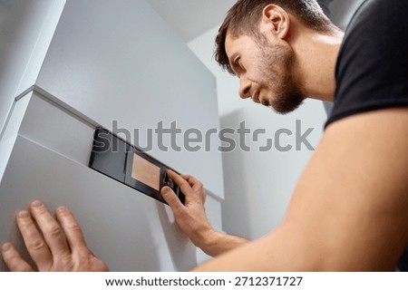 Man adjusting control panel on heat pump inside modern home during installation. Concept of home heating, energy efficiency and HVAC maintenance