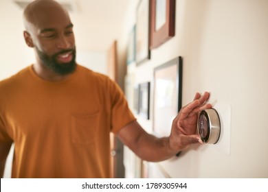 Man Adjusting Digital Central Heating Thermostat At Home