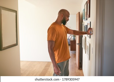 Man Adjusting Digital Central Heating Thermostat At Home