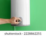 Man adjusting electric boiler on green wall, closeup