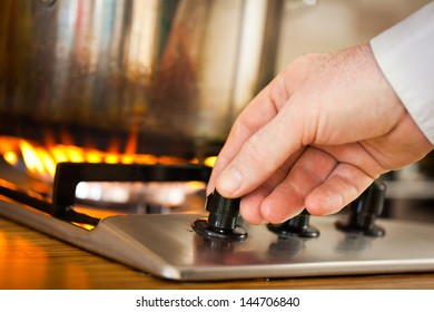 A Man Adjusting The Flame On The Top Burner Of His Stove.