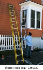 Man Adjusting Ladder Painting Outside Of House