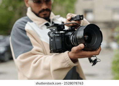 Man adjusting settings on a high-end camera during outdoor shoot, focusing on capturing the perfect shot Wearing casual attire and concentrating on the task - Powered by Shutterstock