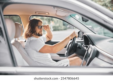 Man adjusting sunglasses inside a modern car, looking outside thoughtfully - Powered by Shutterstock