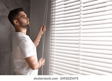 Man adjusting window blinds at home, space for text - Powered by Shutterstock