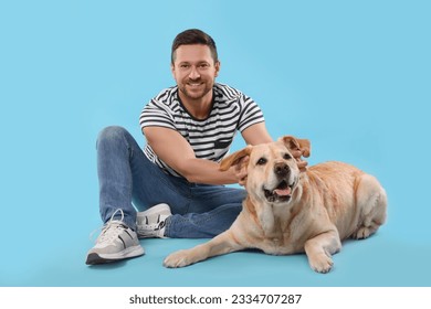 Man with adorable Labrador Retriever dog on light blue background. Lovely pet