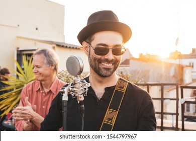 Man In Adult Age Performing On A Rooftop At Summer Season. Music Live Concerts Concept. Lead Singer Of A Rock Band Singing A Song. Portrait Of A Hipster Male Musician Playing On An Intimate Concert.
