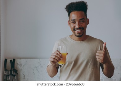 Man Of African American Ethnicity In Casual Clothes Drink Orange Juice Show Thumb Up Eat Breakfast Muesli Cereals With Milk Fruit In Bowl Prepare Cook Food In Kitchen Home Indoor. Healthy Diet Concept