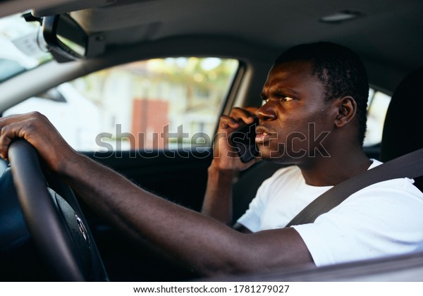 Man of African\
appearance driving a car talking on the phone professional\
communication official