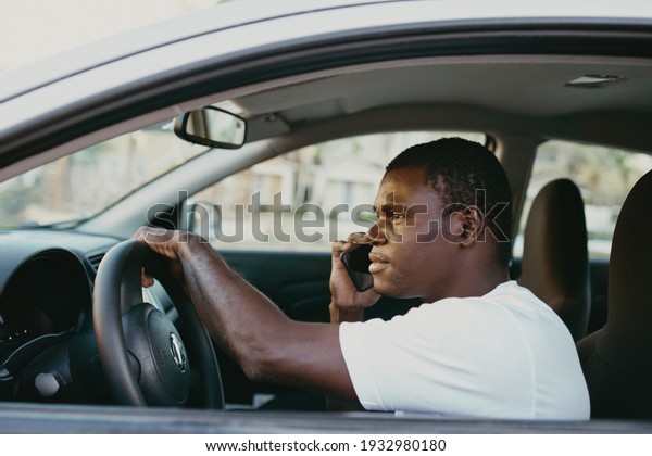 man of african appearance driving a car talking on\
the phone trip