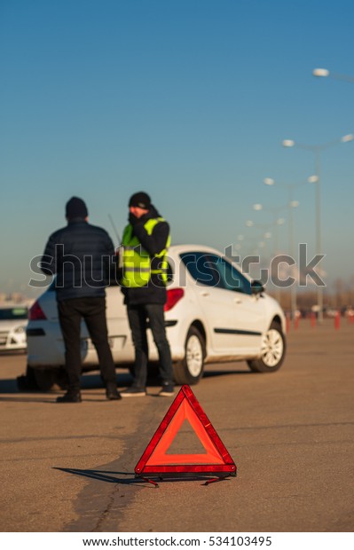 Man after car breakdown and\
car assistance technician on parking. Red triangle sign on\
foreground.