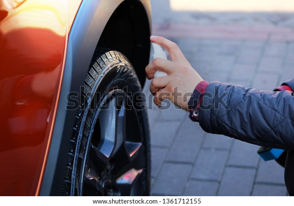 Man after\
washing applies tire cleaner with a white spray. Orange car at car\
wash. Male hand and car wheel close\
up.
