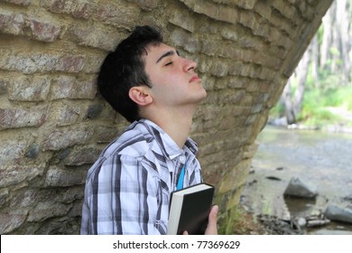 Man Against Wall Holding Bible To Chest With Closed Eyes