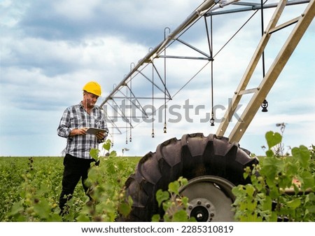 Man agriculture expert, farmer standing near watering systems on the field with digital tablet 