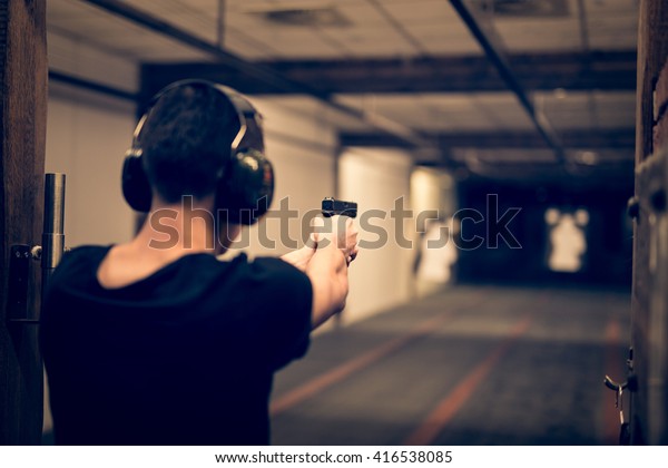 Man aiming pistol at target in indoor firing range\
or shooting range