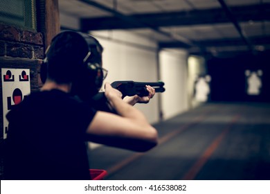 Man Aiming Shotgun At Target In Indoor Firing Range Or Shooting Range