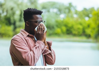 Man with allergy or an infection sneezing. Shot of a young man blowing his nose outdoors. His immune system needs a booster. Hipster man Sneezing. 