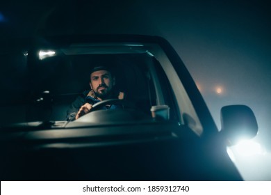 The Man Is Alone Driving A Car At Night. Young Serious Focused Guy Is Driving In A Car Driving Late At Night In The Dark