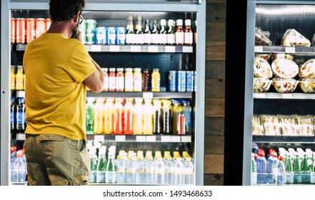 man alone and isolated at the supermarket or minimarket choosing his drink or snack in big fridge with lots of products - difficult select and choose