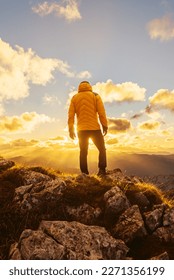 man alone on his back in a yellow jacket on a mountain peak contemplating the sunset in the backlight. Mountaineer contemplating the landscape after hiking in the mountains