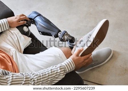 Man amputee with prosthetic leg disability on above knee transfemoral leg prosthesis wearing shoe sitting on sofa, close up. People with amputation disabilities everyday life concept.