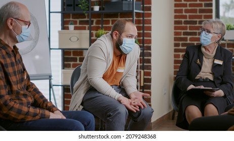 Man With Anger Manangement Issues Talking To Psychiatrist At Aa Therapy Session, Wearing Face Mask. Angry Person Having Conversation About Mental Health Problems At Rehab Meeting.