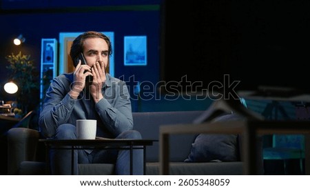 Man appalled by upsetting breaking news story on TV, doing phone call to family member. Person at home scared by troubling events broadcasted on TV, calling friend using smartphone, camera B