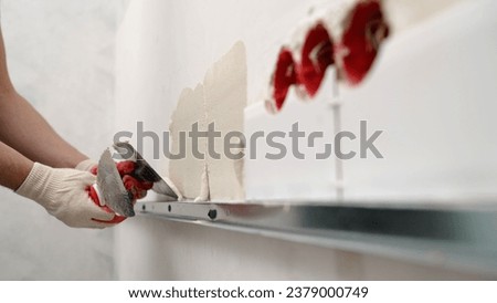 A man applies adhesive to a wall using a tile spatula. Wall cladding. The hands of a craftsman apply tile adhesive to the walls using a spatula.