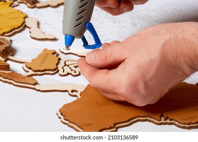 A Man Applies Glue With A Hot Glue Gun To A Model Of The Country.