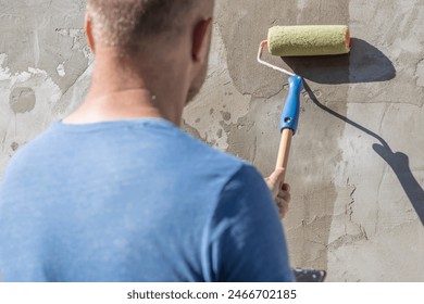 A man applies primer to a concrete wall using a roller. The image shows the process of painting exterior walls, highlighting the techniques and equipment used. - Powered by Shutterstock