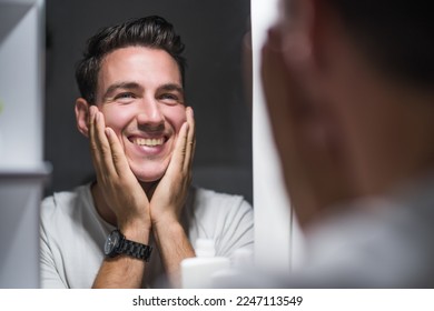 Man is applying aftershave while looking himself in the mirror.