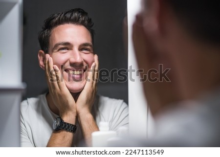 Man is applying aftershave while looking himself in the mirror.