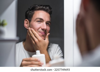 Man is applying aftershave while standing  in front of mirror.