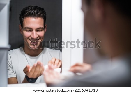 Man is applying aftershave while standing  in front of mirror.