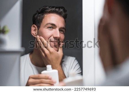 Man is applying aftershave while standing  in front of mirror.