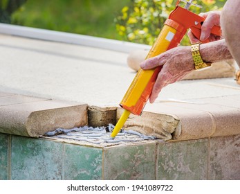 Man Applying Cement Adhesive With A Caulk Gun Tool. Repairing Broken Concrete Paver Stone Swimming Pool Tile.