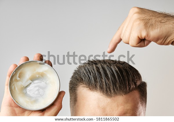 Man applying a clay, pomade, wax, gel or mousse from
round metal box for styling his hair after barbershop hair cut.
Advertising concept of mans products. Treatment and care against
lost of hair